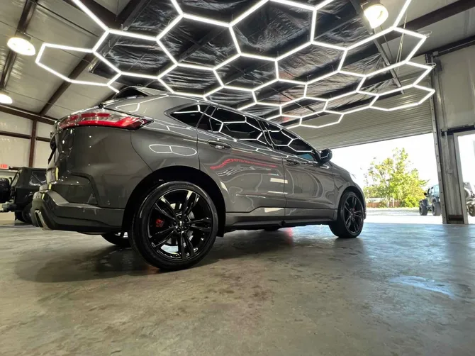 A gray car is parked in a garage under a honeycomb ceiling.